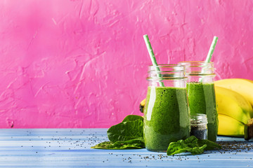Green smoothies in glass bottles on cool pink blue background with yellow bananas, selective focus - obrazy, fototapety, plakaty