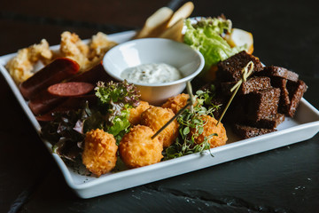 Meat plate with pork ribs, chicken, fried potatoes, cheese balls, croutons, sausages with sauce on black background