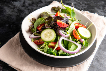 Vegetable salad with fresh lettuce, tomatoes and cucumber in white plate on black background