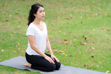 Fototapeta na wymiar Young woman kneels on the mat in the park to prepare for yoga.