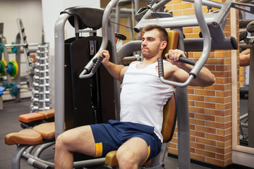 Fototapeta na wymiar Man exercising at gym. Fitness athlete doing chest exercises on vertical bench press machine
