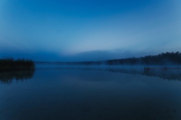 Fototapeta na wymiar Fog over the lake, twilight over the lake, very dense fog, dawn, blue sky over the lake, the morning comes, the forest reflects in the water, surface water, clear morning sky, gothic, Grim picture