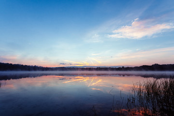 Beautiful, pink violet dawn over the lake. Fog over the lake, the rays of the sun, very dense fog, dawn, the blue sky over the lake, the morning comes, the forest reflects in the water.