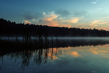 Beautiful, red dawn on the lake. The rays of the sun through the fog. The blue sky over the lake, the morning comes, the sky is reflected in the water.