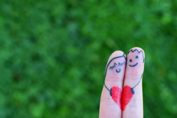 Two fingers as happy couple in love with funny painted smiley faces holding red heart and smiling...