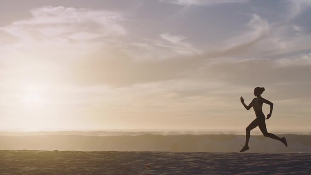 silhouette woman athlete runner on beach running waves splashing female exercising sprinting intense workout on rough ocean seaside at sunset