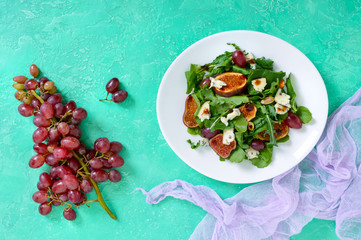 Classic salad with figs, arugula, blue cheese, grapes on a white plate. Tasty vegetarian dish. The top view