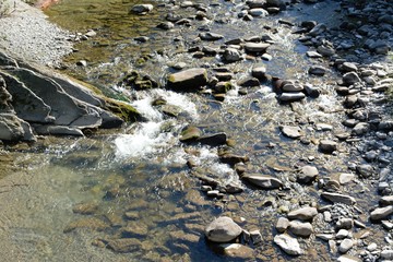 Crystal water river with rocks running through the mountain under the sunshine