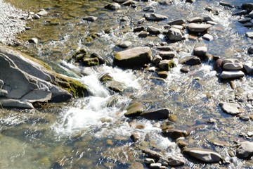 Mountain river running along through rocks with crystal water under the sunshine