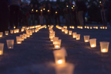 A group of candles burning in street and people holding candles in the background. Day of Memory of the Bereaved