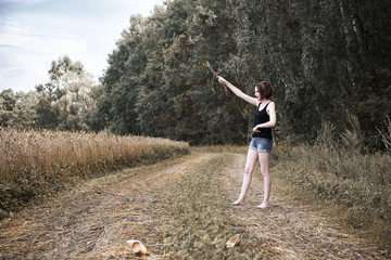 Fototapeta premium young girl walking barefoot on the ground road through field and forest, the concept of summer and travel