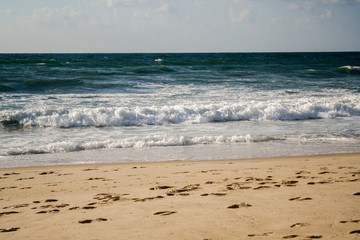 Seascape, blue waves with white foam on the beach with golden sand under a blue sky