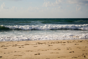 Seascape, blue waves with white foam on the beach with golden sand under a blue sky