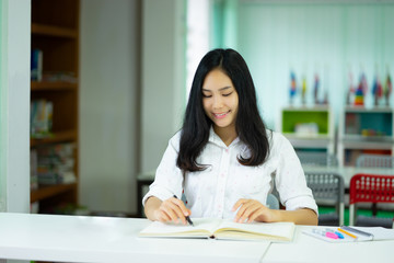 School Education concept, young Asian student  studying and reading test book at library, Asia half Blood Thai Chinese school girl study English, She makes a note on notebook preparing homework exam