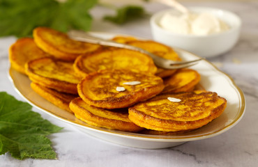 Homemade pumpkin pancakes served with sour cream on a light background.
