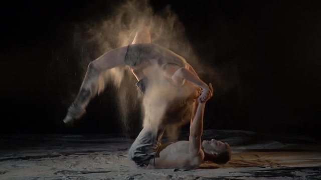 A bearded man and a woman in the Cretaceous perform tricks of acro yoga, slow motion