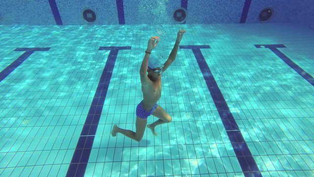 The teenager swims in the pool under the water.