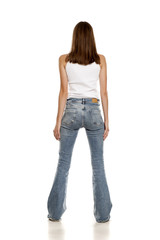 Back view of young pretty woman posing in bell bottom jeans on white background