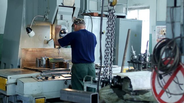 A man specializes a driller drilling holes on a drilling machine in a metal workpiece, a small business, private workshop, perforator