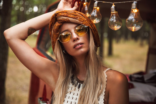 Photo of beautiful hippie woman, wearing stylish accessories looking forward while resting in forest camp