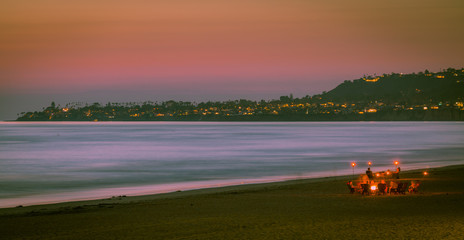 Fototapeta premium There is nothing quite so captive as watching the sun go down while strolling along the beach. Everybody seems to stop what they are doing to take in the beautiful colors of the sky and ocean waters 