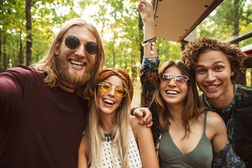 Photo of laughing hippie people men and women taking selfie in forest near retro minivan