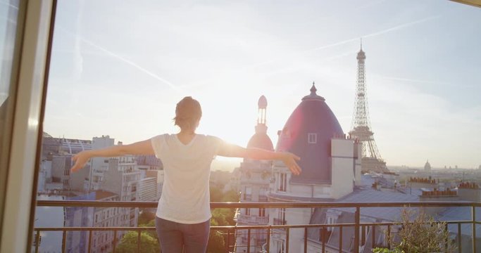 young happy woman tourist arms raised celebrating successful travel vacation enjoying independent freedom relaxing on balcony at sunset in paris france looking at eiffel tower