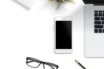 Phone beside laptop on office desk. Blank screen for mockup. Free space beside for text.