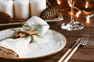 Thanksgiving table setting among white candles and cones. Ceramic plate with fork and knife on a...