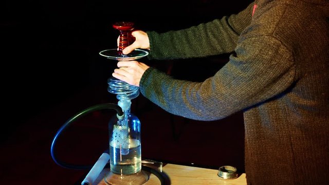 Hookah master prepares hookah. Puts bowl on top of hookah