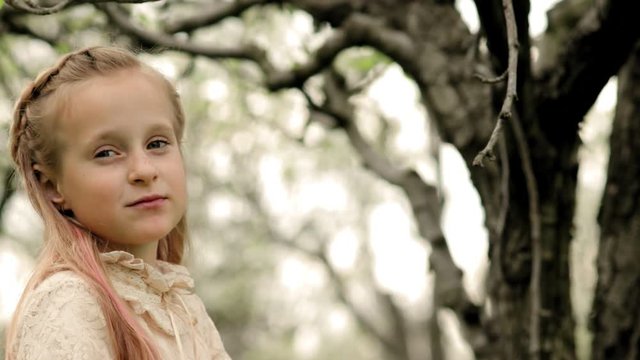 Little girl with pink earlock in a vintage dress chewing an apple in a garden in slow motion