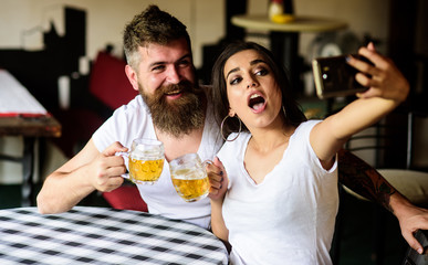 Couple cheerful mood drinking beer in pub. Man bearded hipster and girl with beer glass full of craft beer. Couple in love on date drinks beer. Take selfie photo to remember great date in pub