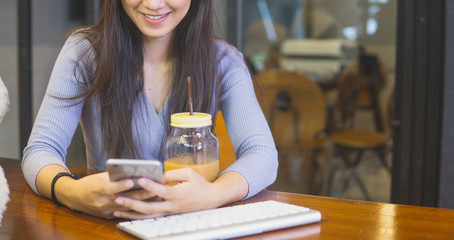 Beautiful young asian woman in the cafe, using mobile phone and drinking coffee smiling.