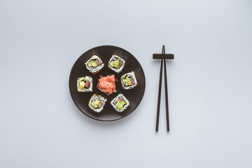top view of delicious sushi with ginger on round plate and chopsticks isolated on white