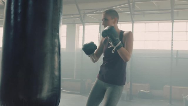 fitness woman athlete training kickboxing exercise workout punching bag strong female fighter practice fierce strength in gym wearing boxing gloves slow motion