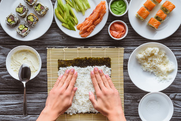 partial top view of person preparing sushi with rice and nori, gourmet ingredients on table
