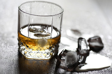 Whiskey in a glass and pieces of ice on a wood