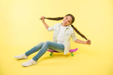 Fototapeta na wymiar Girl show long ponytail hairstyle sit penny board yellow background. Child cute hairstyle ride penny board. Proud of long hair. Hairstyle for active leisure. Keep hairstyle tidy during sport activity