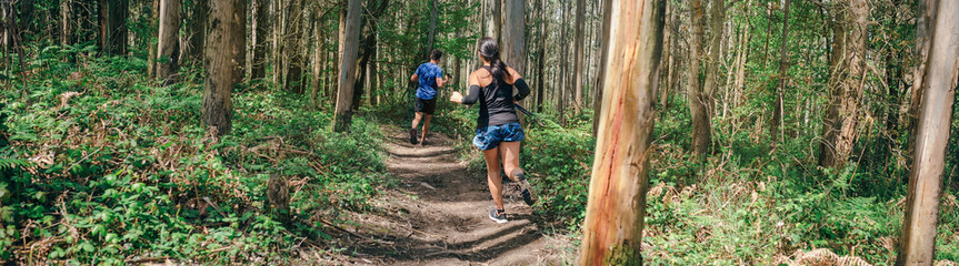 Naklejka na ściany i meble Young woman and man participating in a trail race through the forest