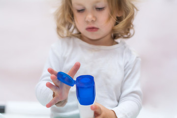 beautiful baby holding a bottle in the hand with shower gel, beside lies Baby cosmetic tubes on white isolated background