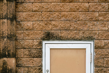 Close up rough brick of prefabricated wall with trash bin door and green algae or Lichen on the wall