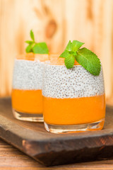 Chia pudding with pumpkin puree in beautiful glasses with green mint leaves and fresh ripe vegetable.