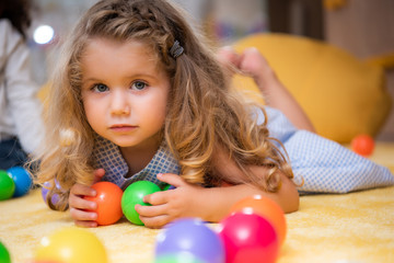 Fototapeta na wymiar adorable child lying on carpet with colorful balls in kindergarten and looking at camera