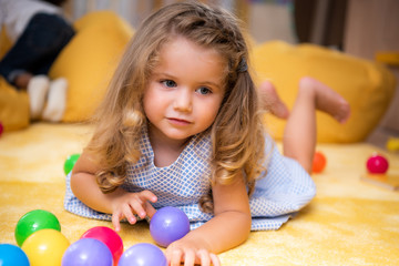 adorable caucasian kid lying on carpet with colored balls and looking away in kindergarten
