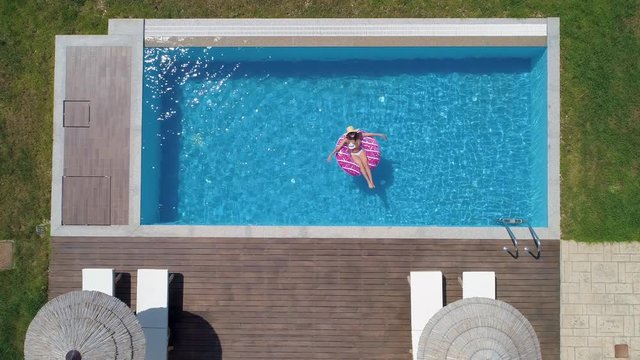 Aerial - Young happy woman relaxing on inflatable donut floatie in the pool