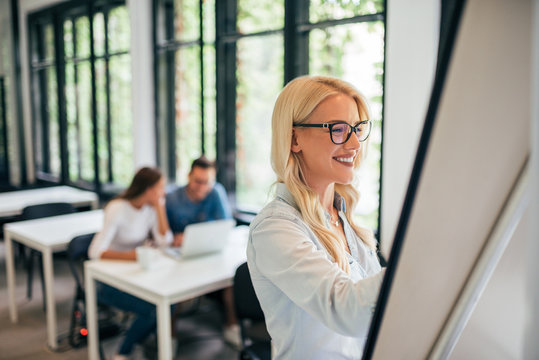 Close-up Image Of Young Blonde Woman Writing On A Whiteboard.