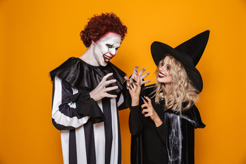 Image of witch woman and joker man wearing black costume and halloween makeup playing around,...