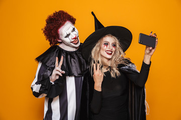 Photo of witch woman and joker man wearing black costume and halloween makeup taking selfie on...