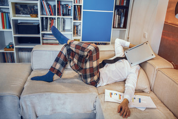 Man sleeping on sofa and holding laptop on head. Relaxing after long work. Business at home concept.