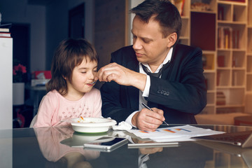 Obraz na płótnie Canvas Father in suit working with papers and feeding daughter. Business at home concept.